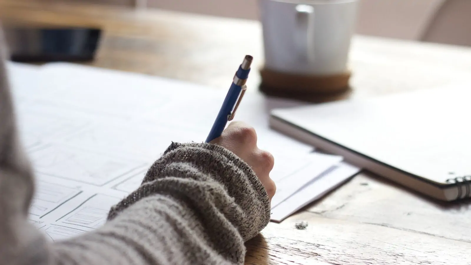 person writing on brown wooden table near white ceramic mug after selecting correct student loan with best grace period 